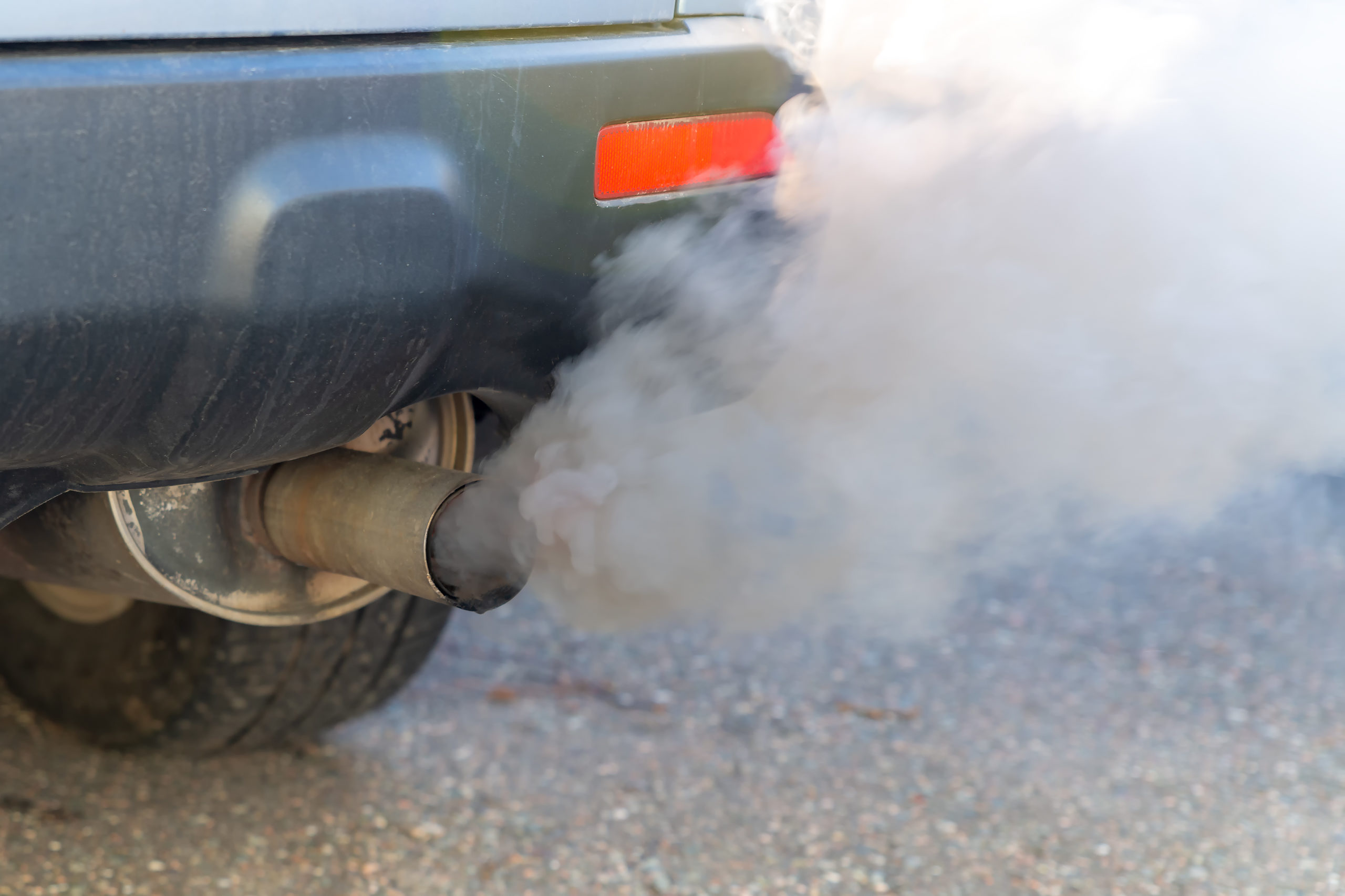 Thick smoke pours from the exhaust pile on a car. Shallow depth of field, focus on the end of the tail pipe. Closeup view.