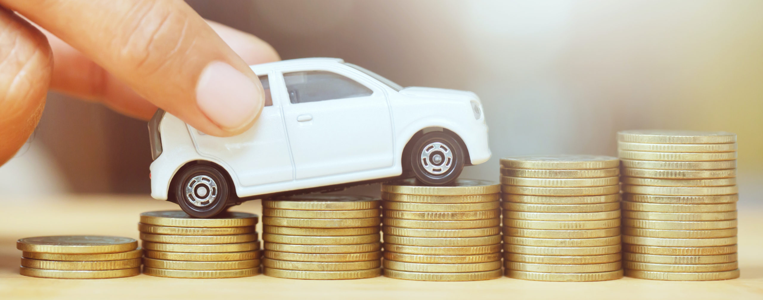 Business man and close up hand holding model of toy car on over a lot money of stacked coins - insurance, loan and buying car finance concept. buy and installments down payment a car.